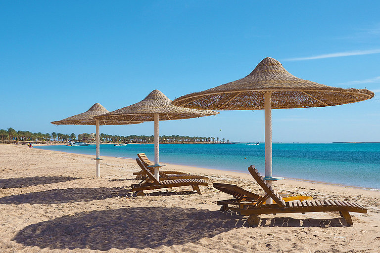 Sandstrand in Soma Bay bei Hurghada mit Sonnenschirmen und blauem Roten Meer.