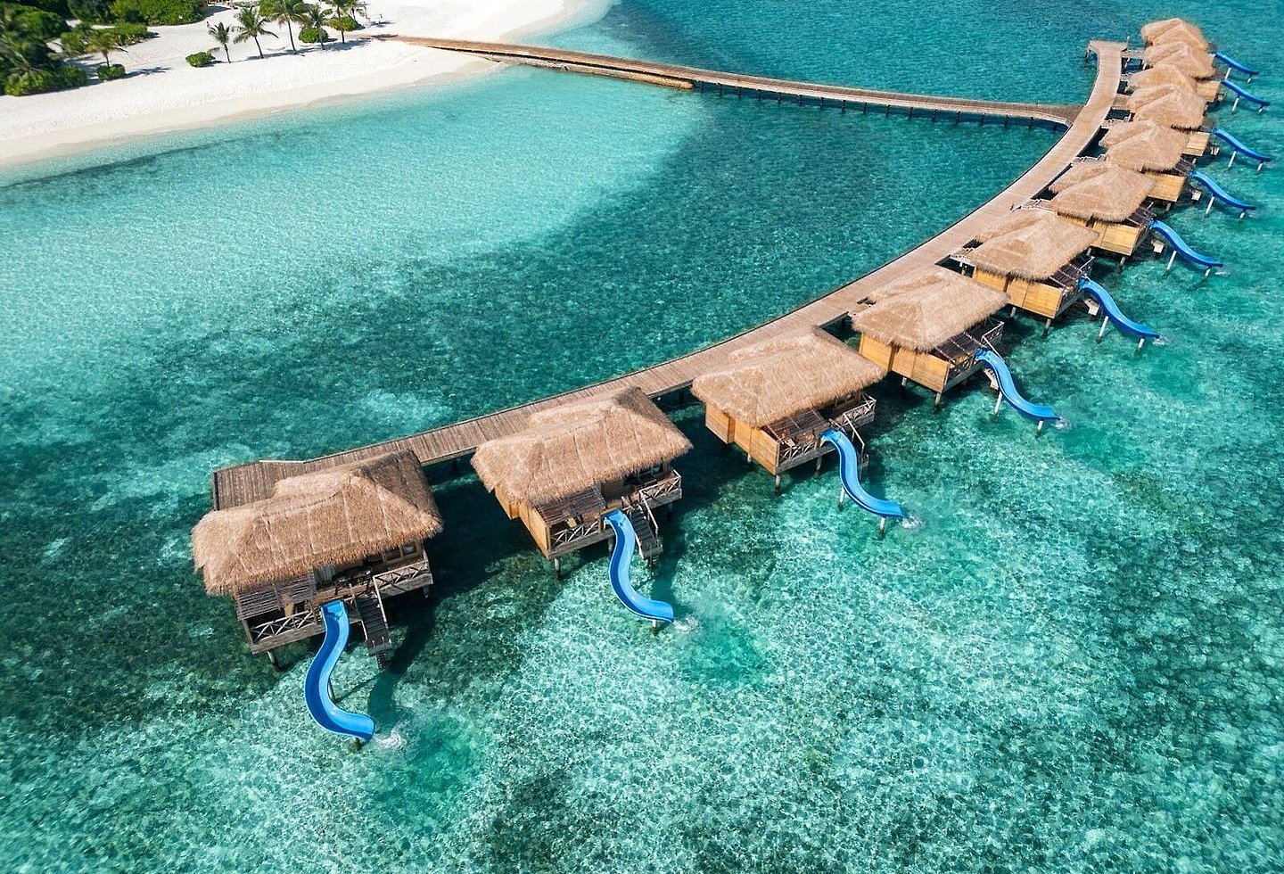 Geschwungene Stege mit Bungalows über kristallklarem Meerwasser.
