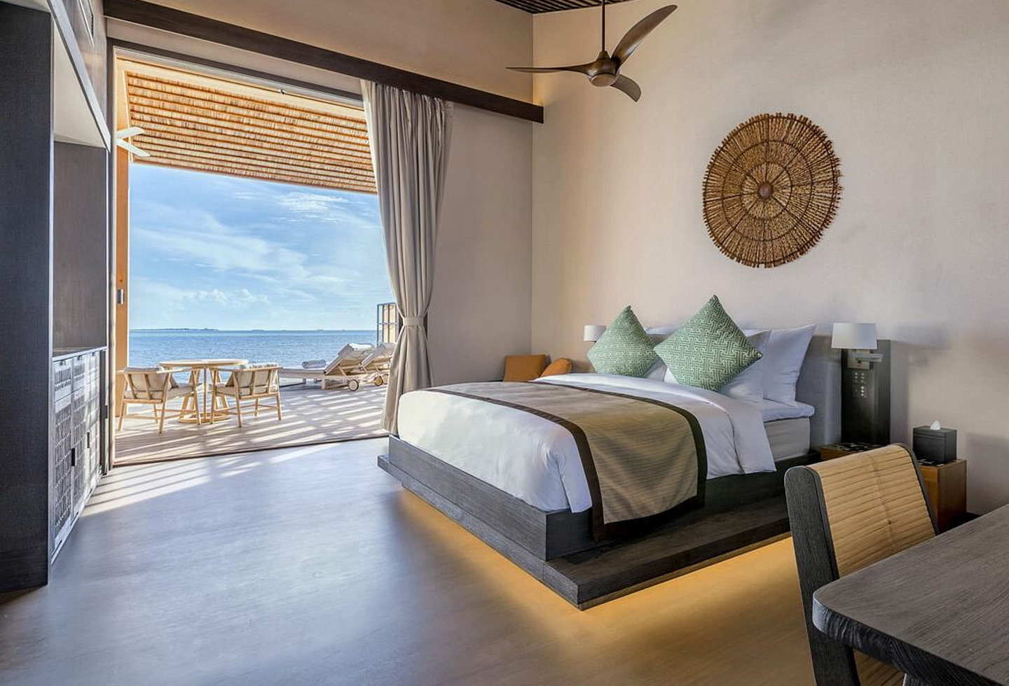 Modernes Zimmer mit Schreibtisch und Bett, Blick auf die Terrasse mit Sitzgelegenheit und Liegen, direkte Sicht aufs Meer