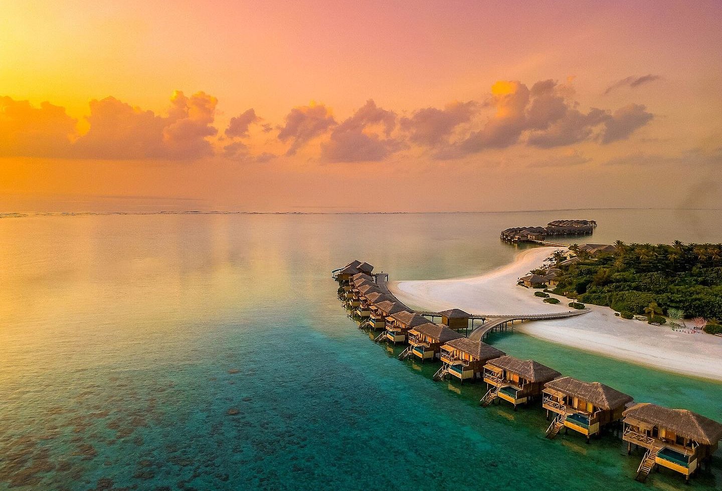 Überwasserbungalows in geschwungener Anordnung bei Sonnenuntergang.