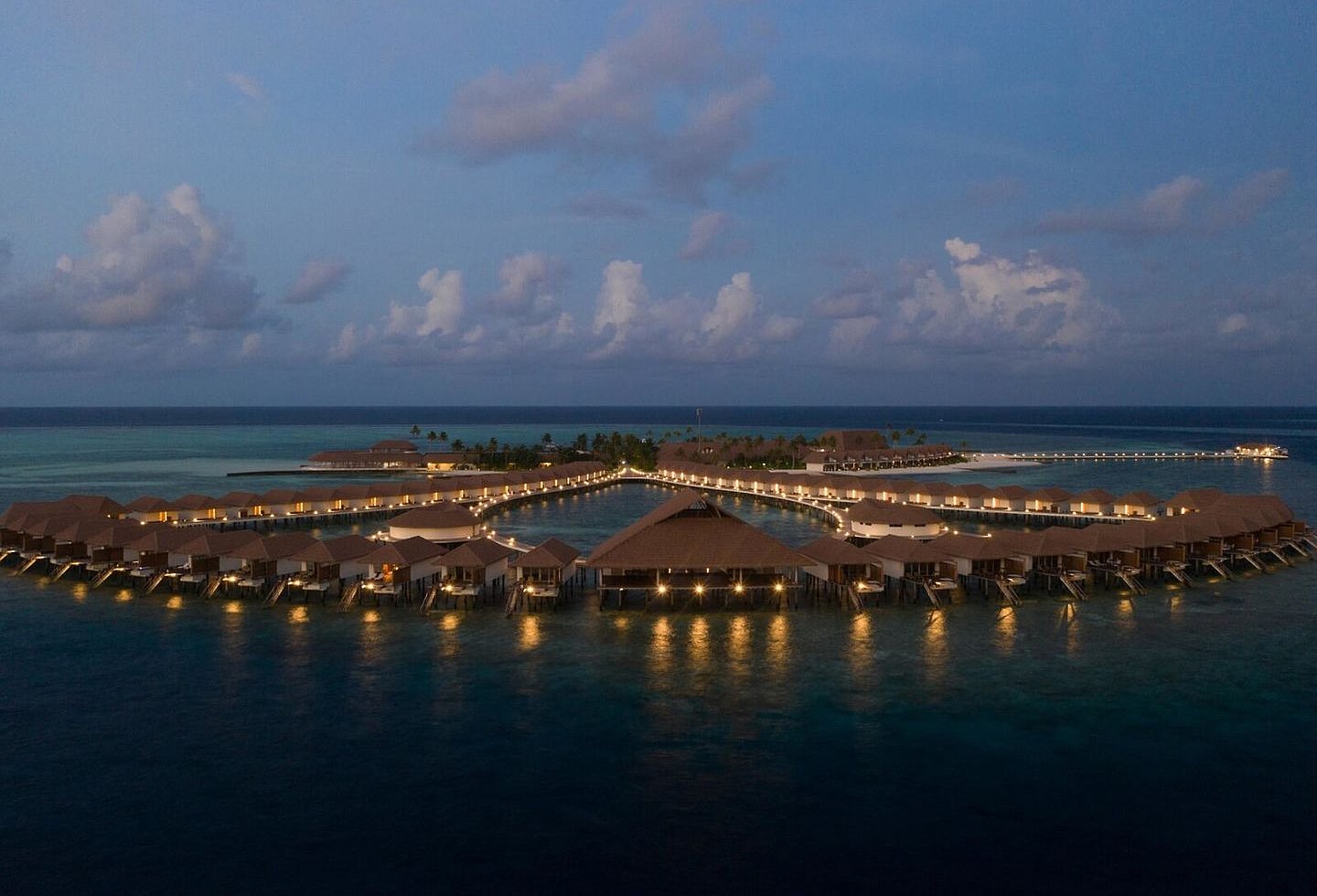 Blick auf ein Resort mit Strandvillen bei Abendlicht und heller Bleuchtung.