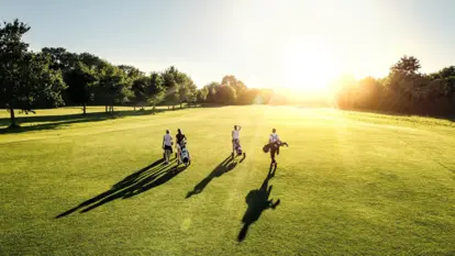 Vier Golfer, drei Frauen und ein Mann, gehen auf einem sonnigen Golfplatz. 