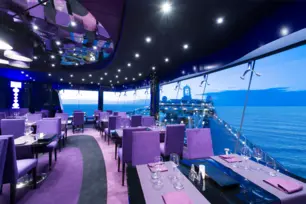 Elegantes Schiffsrestaurant mit violettem Licht, Panoramafenstern und blauem Meerblick.