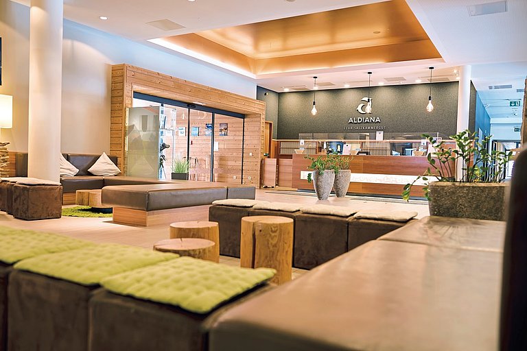 Moderne Hotellobby mit Sitzgruppen, grünen Teppichen und heller Bar.