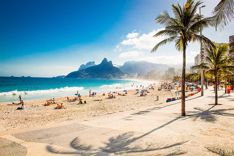 Menschen am Ipanema-Strand mit Blick auf Rios Berge und Palmen
