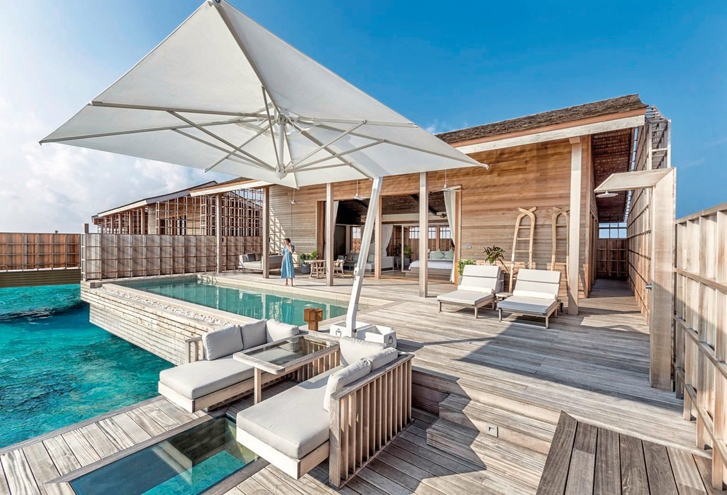 Holzterrasse Villa mit 2 Ebenen, Couchbereich mit Glasfenster zum Meer, auf der oberen Ebene Liegen und Pool sowie großer Sonnenschirm