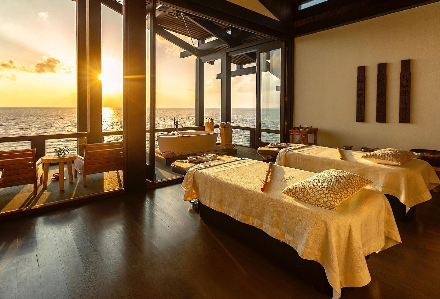 Spa-Behandlungsraum bei Sonnenuntergang, im Innenbereich 2 Liegen, auf der Terrasse freistehende Badewanne und 2 Sessel