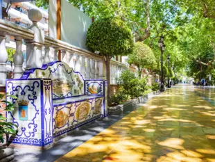 Alameda Park in Marbella mit bunter Keramikbank, Bäumen und gelbem Spazierweg.
