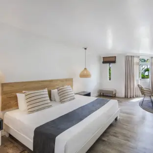 Helles Hotelzimmer mit Doppelbett, gemusterten Kissen und gemütlichem Sitzbereich.
