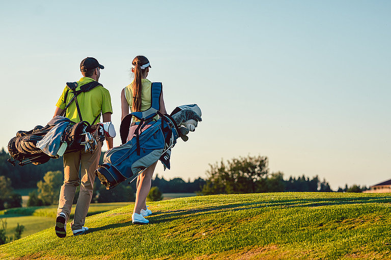 Golfer auf gepflegtem Golfplatz mit Palmen, Fairway und blauem Himmel im Hintergrund.