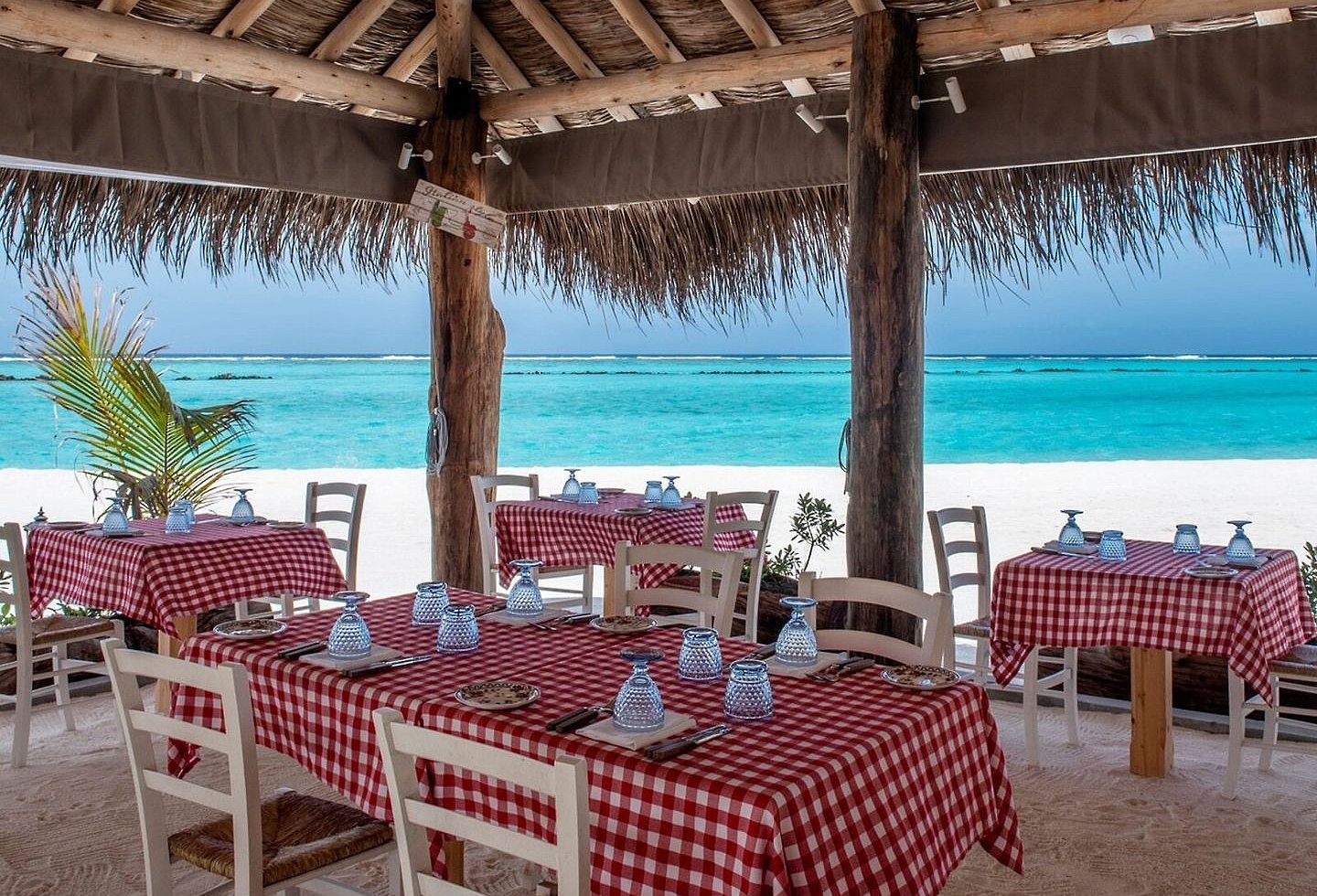 Restaurant mit Blick aufs Meer, gedeckte Tische und schattenspendende Dächer.