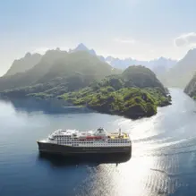 Ein modernes Kreuzfahrtschiff fährt durch eine Lagune mit strahlend blauem Wasser und kleinen Inseln.