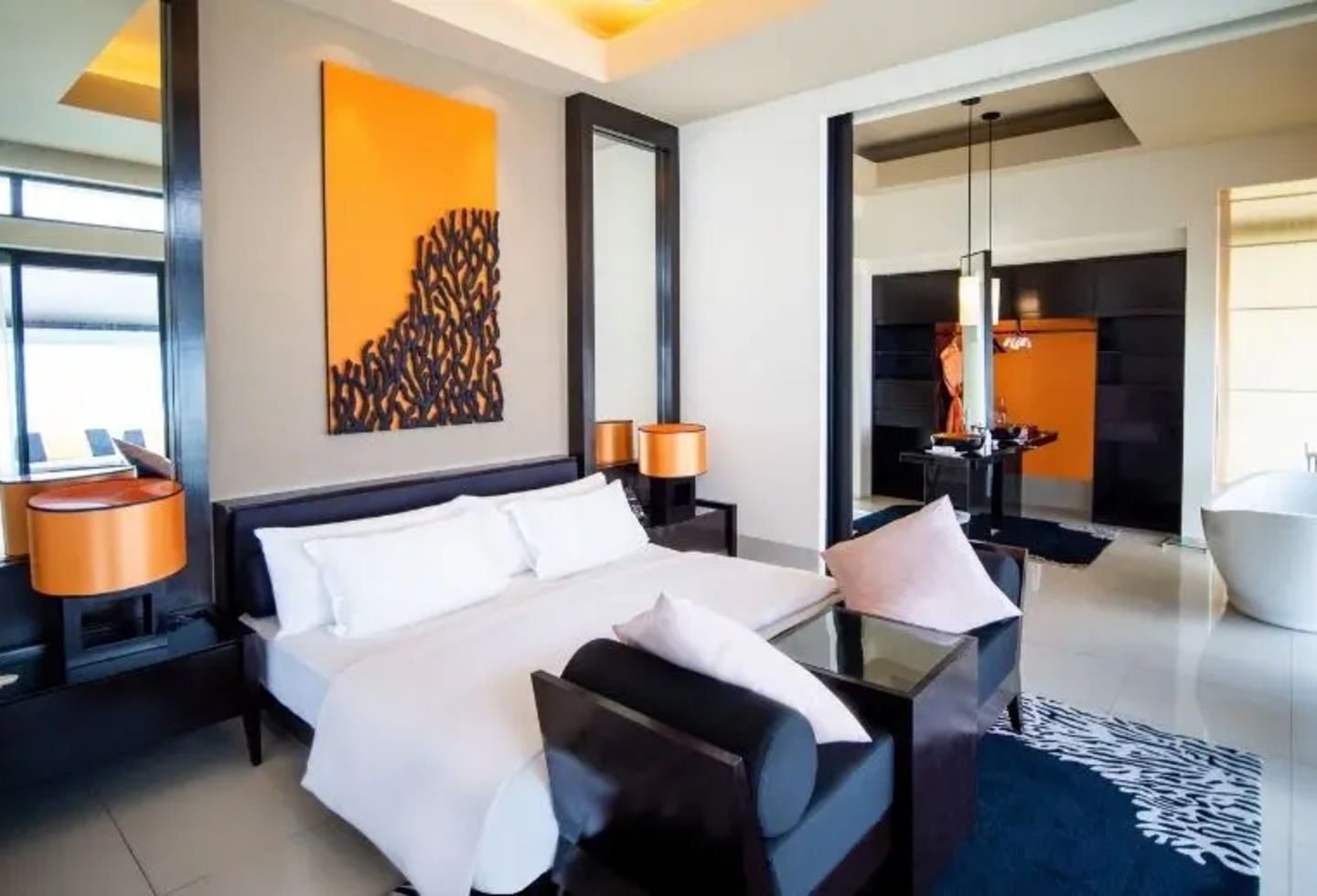 Schlafzimmer mit schwarzen Möbeln, orangen Bild an der Wand, Badewanne im Zimmer.