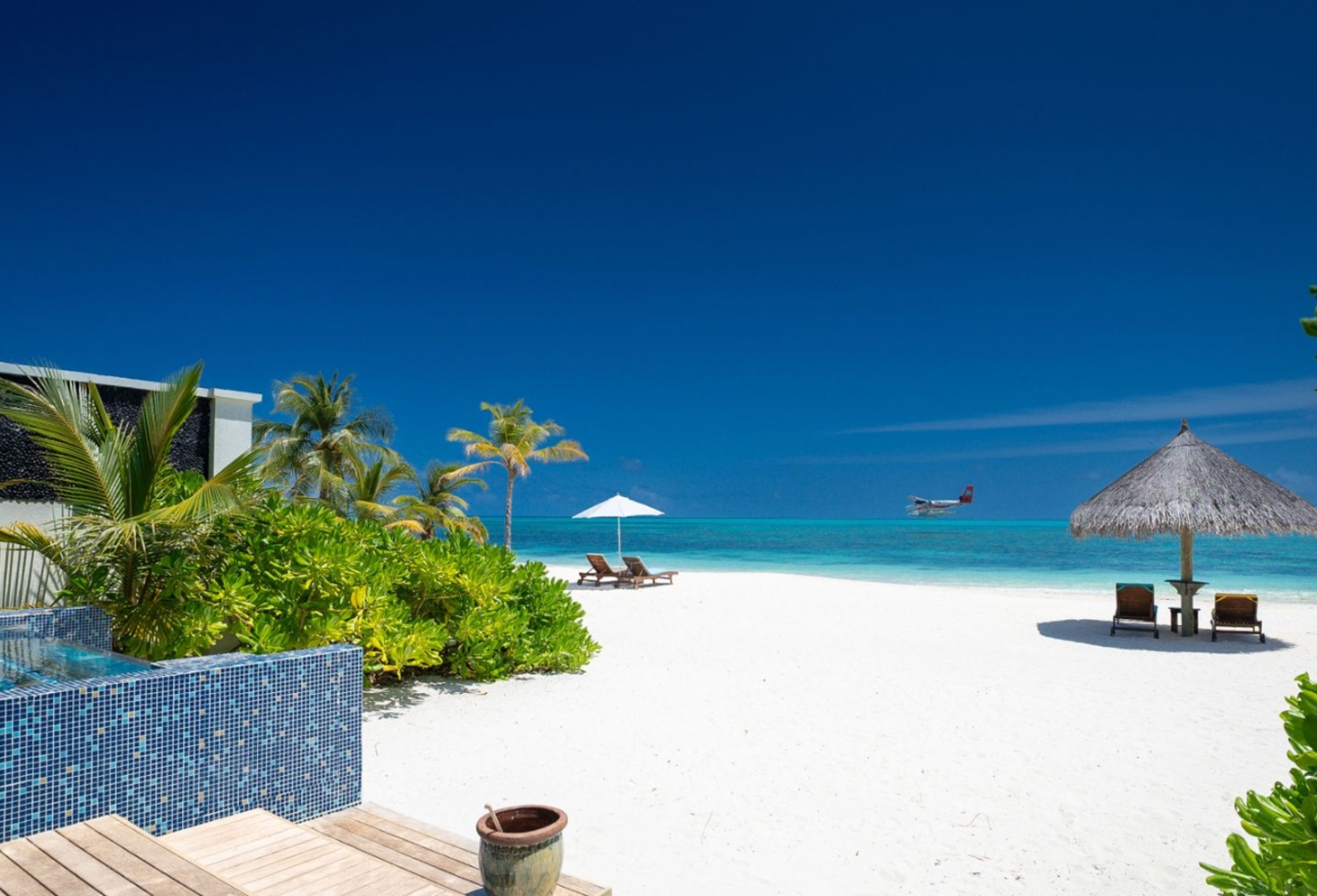 Weißer Sandstrand mit türkisblauem Meer, Palmen und schattigem Strandpavillon.