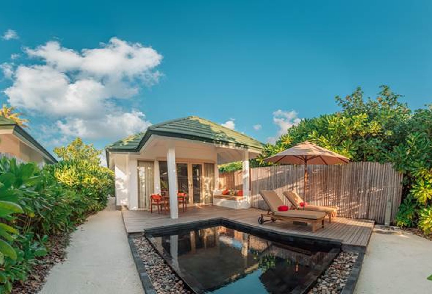 Außenansicht weiße Villa, grünes Dach, Pool schwarz eingefasst, Terrasse mit Liegen