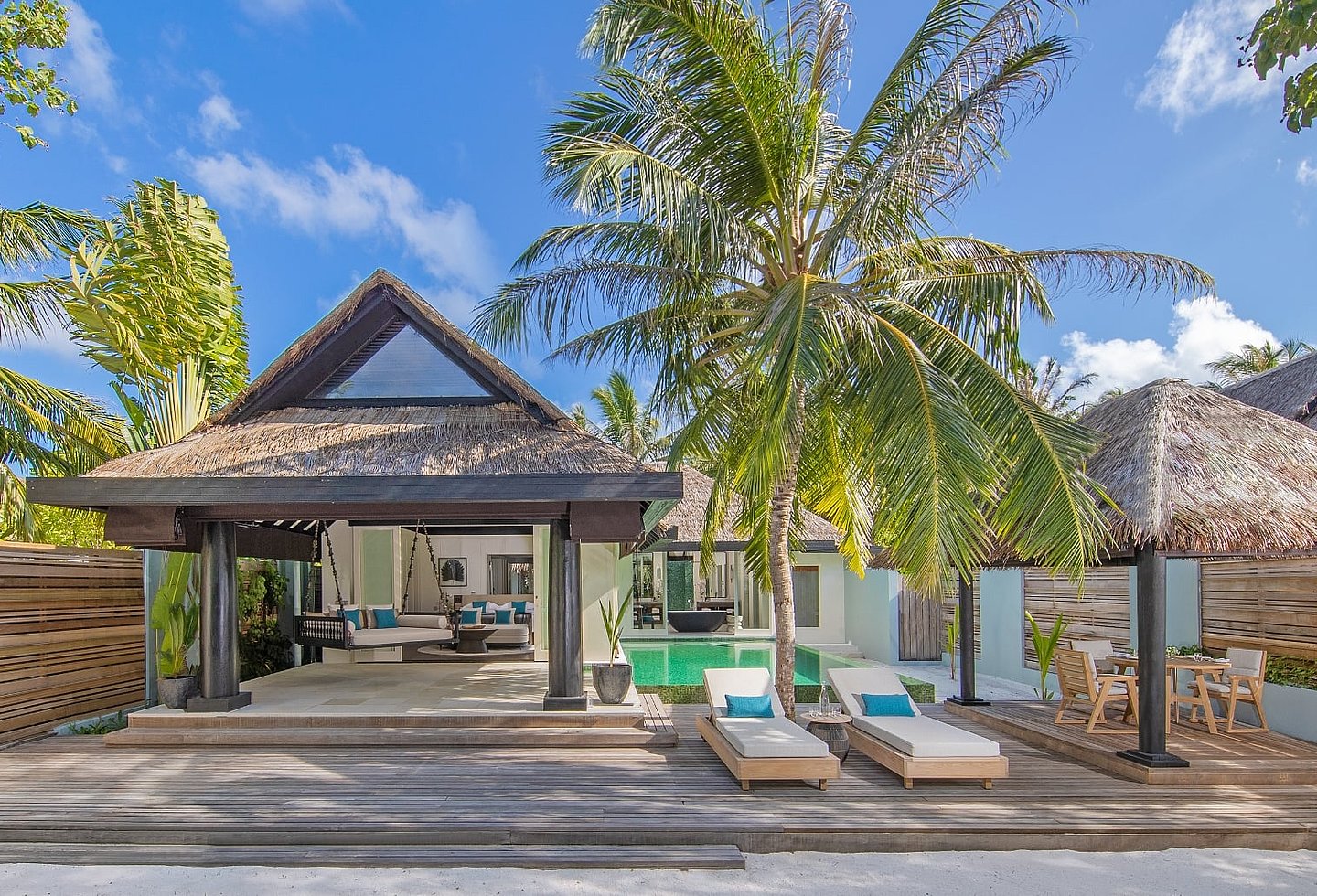 Eingangsbereich eines tropischen Resorts mit Reetdach, Bäumen und blauem Himmel.