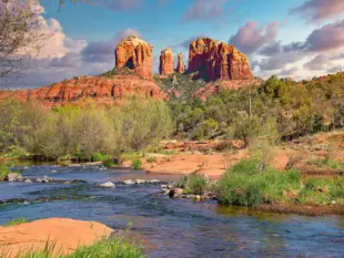 Rote Felsformationen bei Sedona mit Bachlauf und grüner Vegetation im Vordergrund.