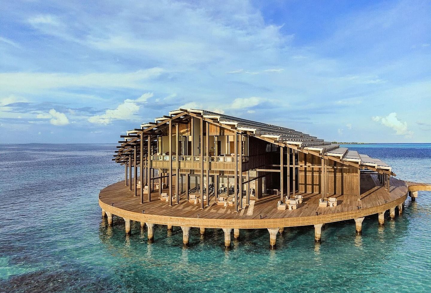 modernes Gebäude auf runder Holzplattform im Wasser, Sitzmöglichkeiten großzügig auf Terrasse verteilt