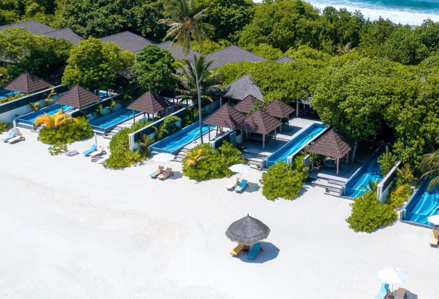 Blick vom weißen Sandstrand zu den Villen mit privaten Pools und Liegen.