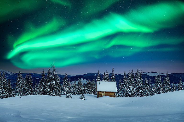 Grüne Nordlichter über verschneiter Winterlandschaft mit Hütte in Norwegen