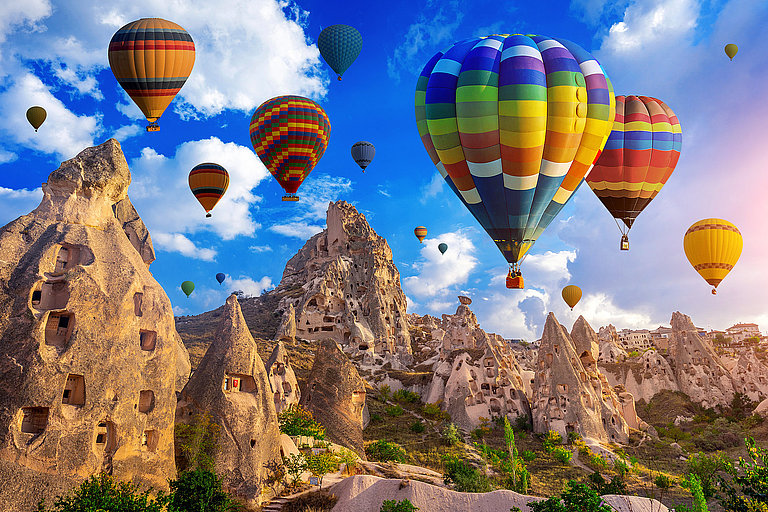 Heißluftballons über Felsformationen in Kappadokien bei blauem Himmel.